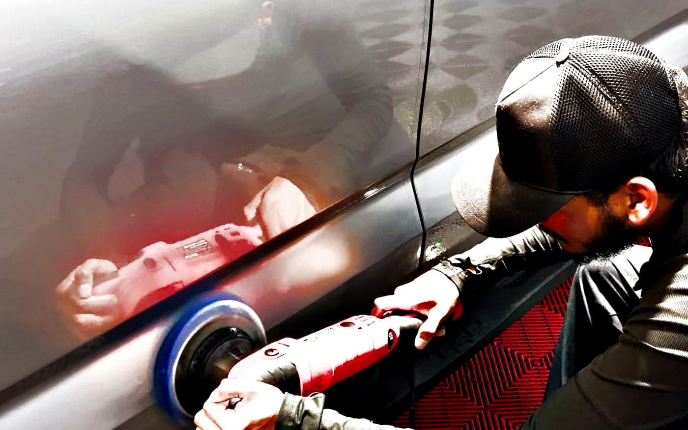 A machine polisher working the door of a silver Tundra, the red tool mirrored in the paint