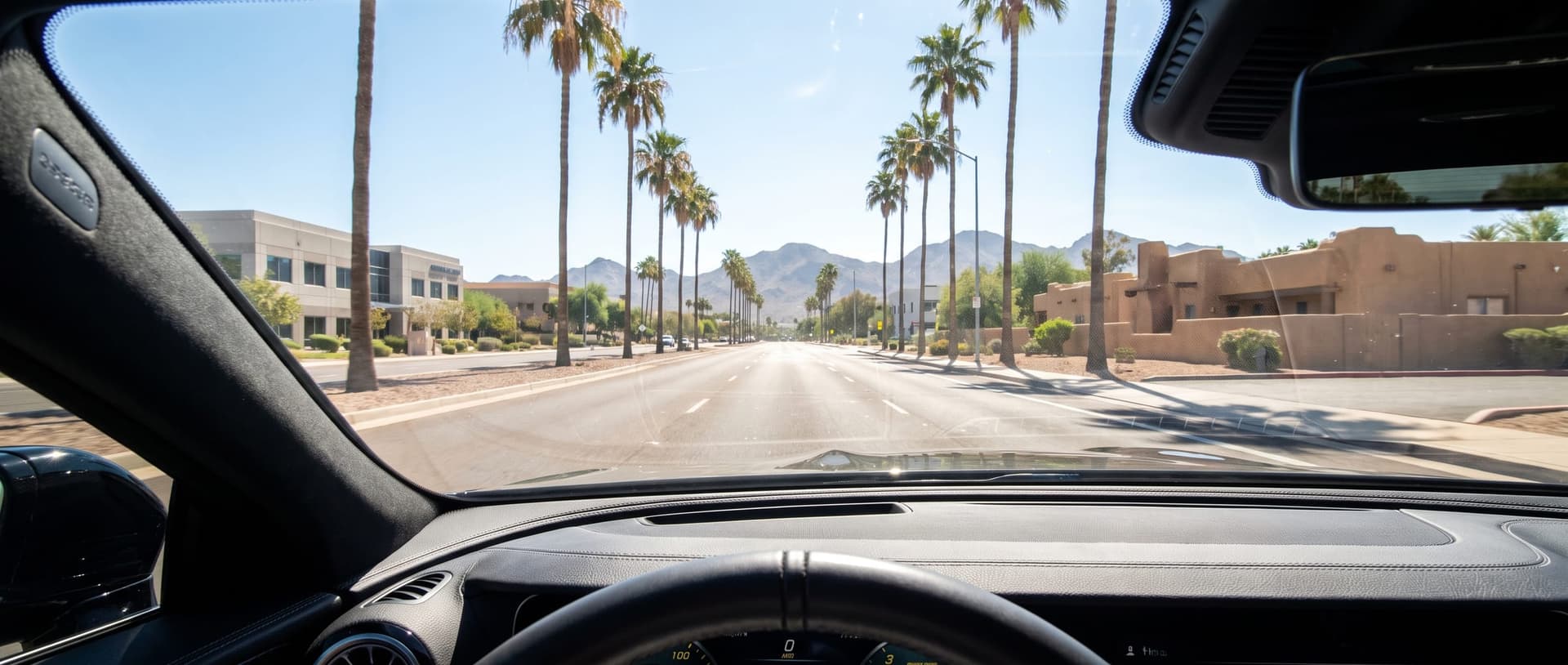 A bright Phoenix street in full sun, seen from the driver seat through the windshield